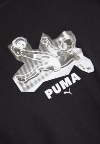 Juodas audinys su balta grafika, vaizduojančia futbolininką judesyje, o po ja dideliu šriftu parašyta "PUMA".