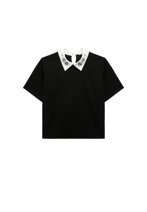 Zwart T-shirt met korte mouwen met een witte kraag met decoratieve versieringen en een sleutelgat sluiting aan de achterkant. Gladde stof, losse pasvorm.