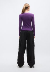 Μακρυμάνικη μωβ μπλούζα σε  συνδυασμό με χαλαρά μαύρα cargo παντελόνια με πολλαπλές τσέπες και ελαστικά τελειώματα. Ομαλή υφή σε όλο το ύφασμα.