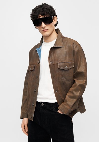 Καφέ δερμάτινο μπουφάν με δύο μπροστινές τσέπες, γαλάζιο γιακά και εφαρμοστή γραμμή. Φορεμένο με λευκό μπλουζάκι και μαύρο παντελόνι.