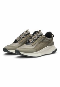 Ett par sport sneakers i beige och svart med texturerad mesh och läder, tjocka vita sulor, logotyp på sidan och svarta snören, vinklad åt höger.
