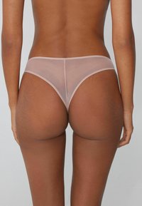 Transparente rosa Netz-Tanga mit minimalistischem Design, ausgestattet mit einem dünnen elastischen Bund und runder Rückendeckung. Weicher Stoff und leichtes Material.