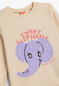 Beige sweatshirt met een ronde hals, voorzien van een paarse olifantgrafiek en de tekst "Sweet Elephant" in het roze en "hello cutie" in het rood.