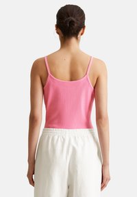 Rosa geripptes Tanktop mit verstellbaren dünnen Trägern, kombiniert mit lockeren weißen Hosen; die Rückansicht hebt die glatte Textur und die figuroptimierte Form hervor.