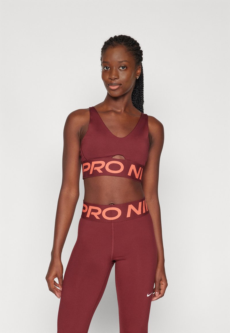 Burgundska športna modra z izrezom, ki ima oranžni pas "PRO NIKE", v kombinaciji z usklajenimi leginami in majhnim belim logotipom.