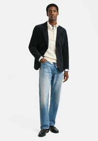 Čierny manšestrový blazer cez krémový sveter s vrkočovým vzorom, svetlomodré džínsy a čierne topánky; s klasickým strihom a štruktúrovanými látkami.