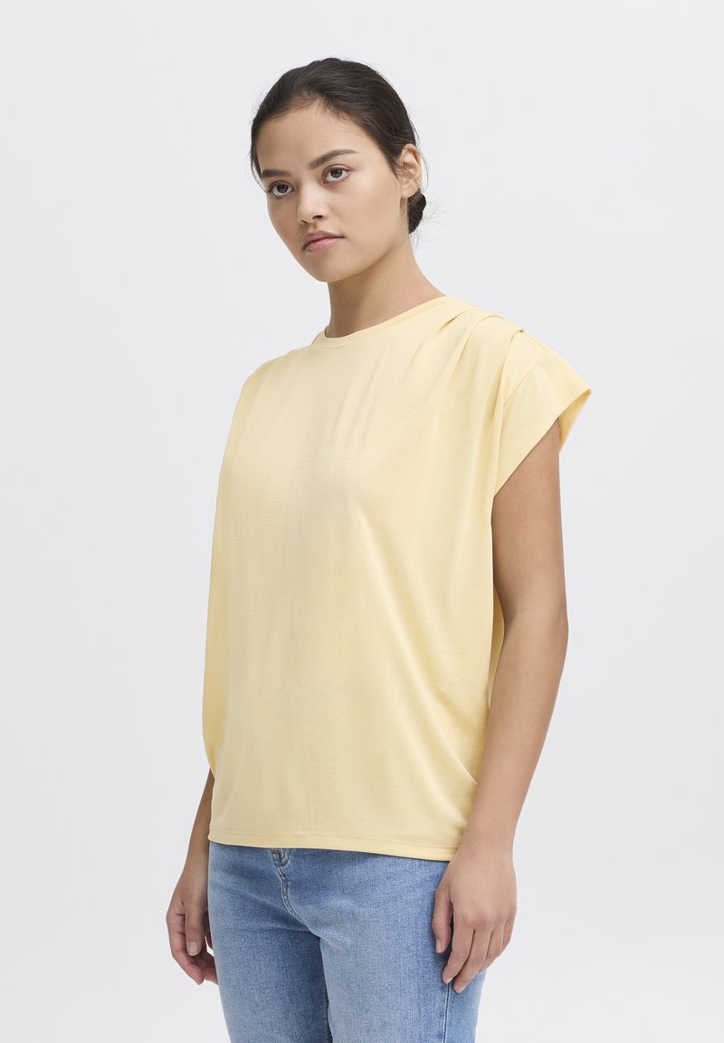 T-shirt giallo a maniche corte con vestibilità rilassata e scollo rotondo, realizzato in tessuto morbido. Presenta una leggera arricciatura alle spalle.
