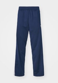 Pantalones de chándal azul marino hechos de una tela suave con cintura elástica. Presentan franjas blancas en los laterales y un pequeño logo en la cadera izquierda.