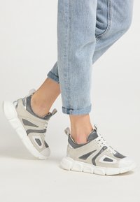 Lekkie buty sportowe z siateczkową cholewką w kolorze szaro-białym, wyposażone w grubą, elastyczną podeszwę i smukłe elementy stylistyczne.