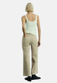 Beige wide-leg corduroy pants with a textured finish, paired with a light tank top. Features two back pockets and a relaxed silhouette.