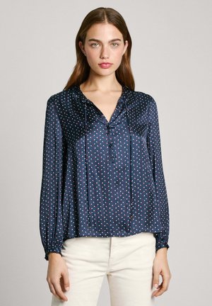 Navy Satinbluse mit langen Ärmeln, V-Ausschnitt, Knopfverschluss und Muster aus weißen und roten Punkte. Mit elastischen Bündchen und lockerer Passform.