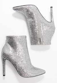 Botines plateados con lentejuelas, punta afilada y tacón de aguja, que cuentan con una cremallera lateral y una textura suave.
