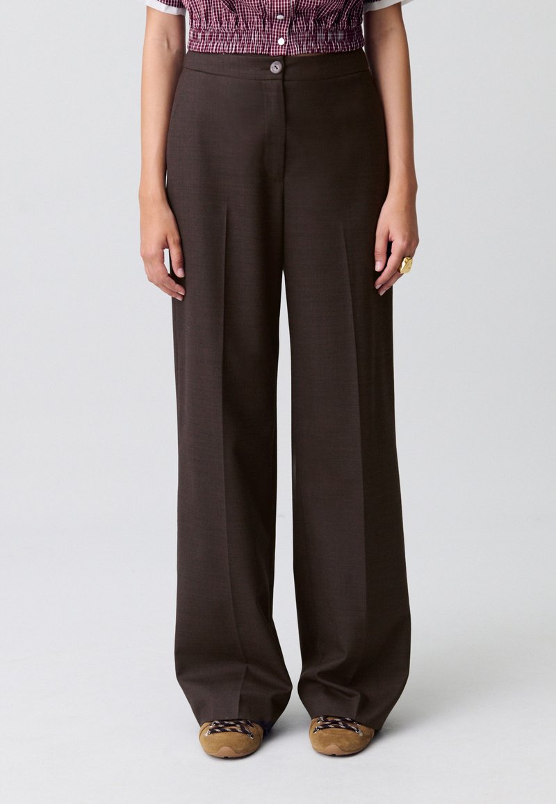 Pantaloni ampi marroni realizzati in tessuto testurizzato, con vita alta e pieghe sottili, abbinati a calzature beige.