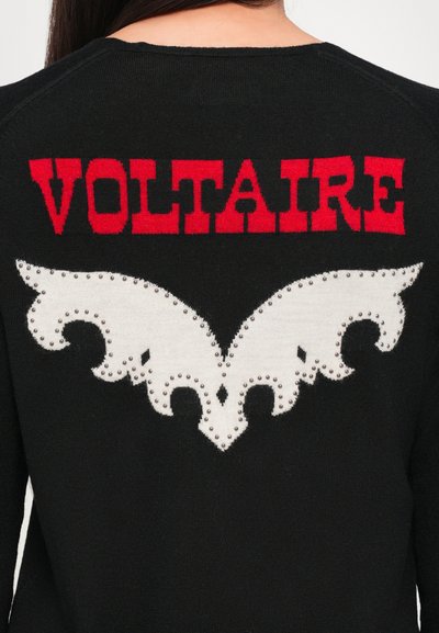 Melnā adīta džemperis ar sarkano "VOLTAIRE" tekstu aizmugurē un baltu dekoratīvo rakstu ar metāla kniedēm.