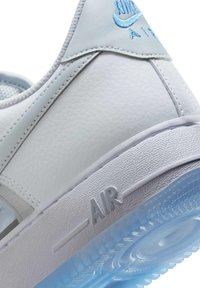 Close-up van de hiel van een witte Nike Air sneaker met lichtblauw geborduurd logo en doorzichtige blauwe buitenzooldetail.