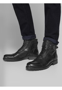 Czarne skórzane botki za kostkę z gładką teksturą, z zamknięciem na sznurówki, bocznym zamkiem błyskawicznym i solidną podeszwą. Zdobione klamrą.