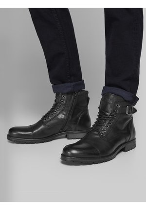 Černé kožené kotníkové boty s hladkým povrchem, disponující šněrováním, bočním zipem a pevnou podrážkou. Ozdobené přezkou.