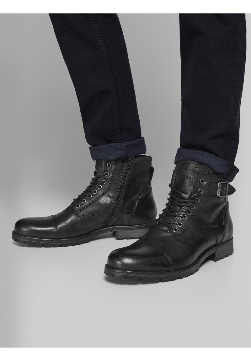 Czarne skórzane botki za kostkę z gładką teksturą, z zamknięciem na sznurówki, bocznym zamkiem błyskawicznym i solidną podeszwą. Zdobione klamrą.