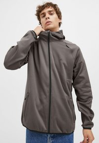 Giacca grigia con zip, dotata di un colletto alto, realizzata in tessuto liscio, con tasche laterali e dettagli in zip nera.