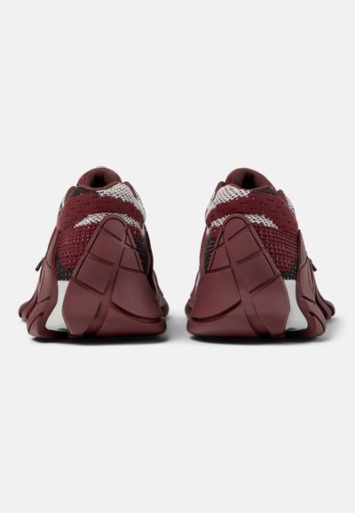 Paire de chaussures de sport bordeaux et blanches vues de dos, avec semelles segmentées et sculptées ainsi que dessus en tissu tricoté.
