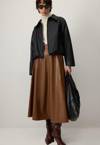 Črna usnjena kratka jakna, bež pulover z zvoncem, rjava midi krilo iz umetnega usnja, rjavi škornji do kolen in velika črna torba.