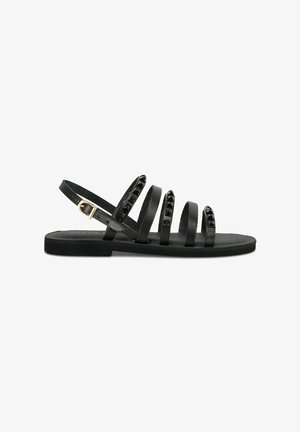 Sandales en cuir noir avec plusieurs fines brides, fermeture à boucle dorée et accents décoratifs en clous noirs sur le dessus. Semelle plate.