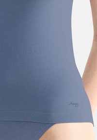 Blauwe stretch stof tanktop met een naadloos ontwerp, met een logo aan de linkerkant en een gladde, zachte textuur.