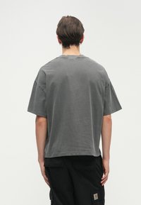 Γκρίζα oversized μπλούζα με κοντά μανίκια, στρογγυλή λαιμόκοψη και μαλακή, υφασματική υφή. Συνδυασμένη με χαλαρές μαύρες cargo παντελόνες, με εμφανή ραφή.