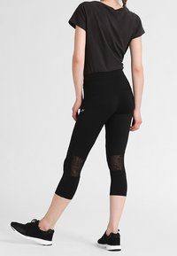 Black athletic leggings with sheer mesh panels and a fitted waist, paired with a short-sleeve, dark top and black athletic shoes.