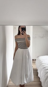 Off-shoulder stribet top i sort og hvid parret med en hvid, svævende midi-nederdel. Blødt stof med subtil struktur og lodrette plisseringer.