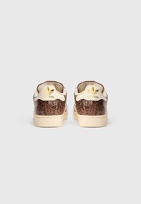Sneakers com textura de pele de cobra castanha e detalhes bejes, apresentando um logotipo dourado no calcanhar. Design clássico de cano baixo com sola em borracha.