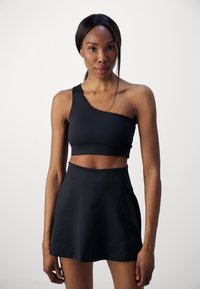 Swar svart en-skulder crop top kombinert med et høydejustert svart skjørt. Glatt tekstur, tettsittende design og minimalistisk stil.