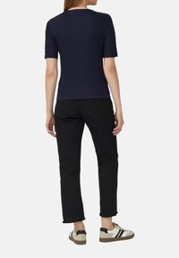 Marineblauwe kortemmers top gecombineerd met zwarte cropped jeans en beige sneakers met zwarte accenten. Zachte textuur; slim fit ontwerp.