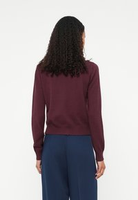 Pullover in magenta a maglia con maniche lunghe e polsini a costine, abbinato a pantaloni blu navy. La texture appare morbida e liscia.