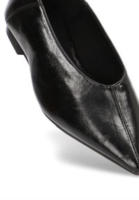 Zapato bajo de piel negra con punta afilada y tacón bajo, con textura suave y costura sutil a lo largo del borde superior.