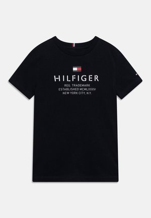Schwarzes T-Shirt mit kurzen Ärmeln und weißem "HILFIGER"-Schriftzug, darüber eine kleine rot-weiß-blaue Flagge sowie zusätzlichem Text mit Verweis auf New York City.
