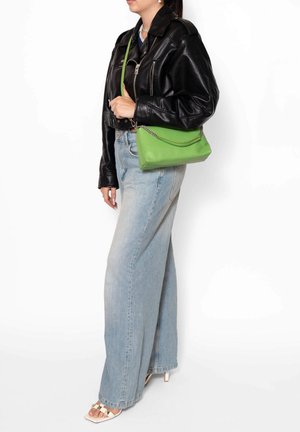 Borsa a tracolla verde in pelle con forma strutturata e dettaglio a catena, esposta insieme a una giacca di pelle nera e jeans a gamba larga blu chiaro.