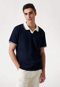 Polo de manga corta azul marino con cuello blanco, que presenta dos rayas blancas. Fabricado en una tela texturada, de corte relajado y con un sutil detalle del logo.