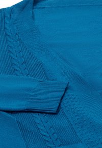 Tyrkysový pletený cardigan s hřejivými manžetami a texturovanými vzory, včetně designu s kabelovým pletením a hladkých ploch.