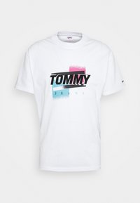 Camiseta de algodón blanca con un logo gráfico en negro, rosa y azul que dice "TOMMY JEANS". Diseño clásico de cuello redondo y mangas cortas.