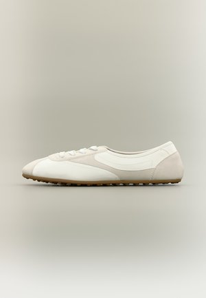 Λευκό sneaker χαμηλού προφίλ με μπεζ λεπτομέρειες και λαστιχένια σόλα, ορατό από το πλάι σε ουδέτερο φόντο.