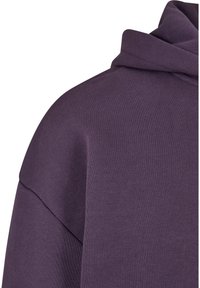 Sweatshirt à capuche violet avec un tissu texturé, coupe décontractée et encolure large à bords arrondis. Coutures visibles en accent.