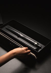 Fer à boucler noir dans un étui noir élégant, doté d'une texture lisse, d'un bouton de contrôle circulaire et d'un accent argenté à la base.