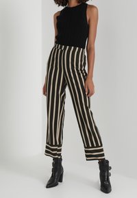 Haut sans manches noir côtelé associé à un pantalon large taille haute à rayures noires et crème. Bottines noires à talons épais avec des brides.