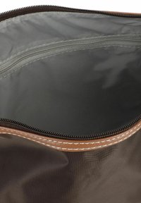 Borsa di stoffa marrone con cerniera, con un esterno liscio e cuciture chiare in contrasto. All'interno ha una fodera grigia impermeabile.