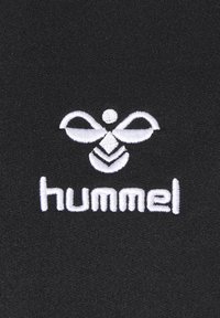 Black fabric with white embroidered logo featuring a stylized bee and the brand name "hummel" in lowercase. Smooth texture.