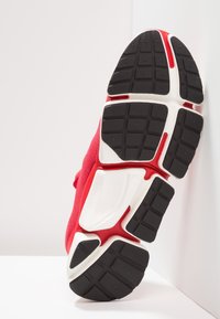 Röd sportskor med en texturerad ovandel, som har en djärv vit mellansula och en svart gummiutsula med rutmönster för grepp.