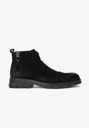 Bottines en suede noir à bout rond, avec un laçage à l'avant et une fermeture éclair sur le côté. Elles possèdent une semelle en caoutchouc texturée avec des profondes trames.