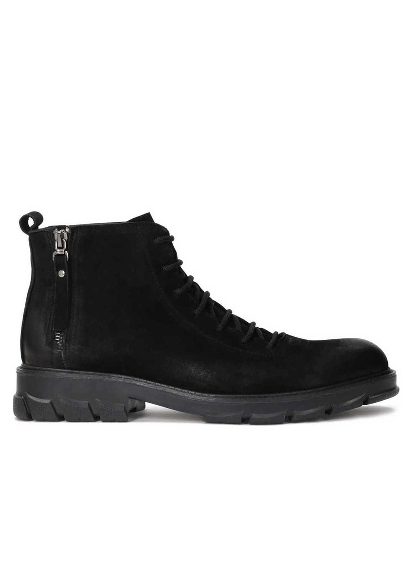 Botas de ante negras a nivel del tobillo con punta redonda, cordones en la parte delantera y cremallera lateral. Presenta una suela de goma texturizada con profundos dibujos.