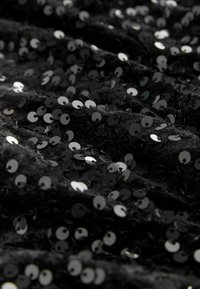 Tissu en sequins noirs avec une texture brillante, featuring de petites paillettes rondes argentées disposées sur un matériau doux et ondulé.